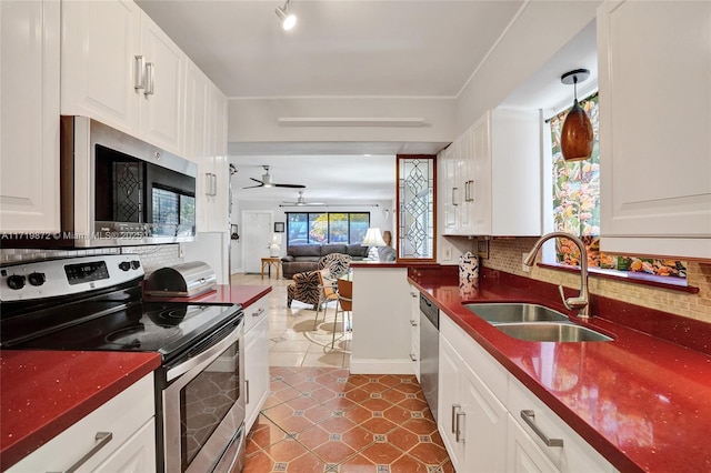 kitchen with appliances with stainless steel finishes, white cabinetry, tasteful backsplash, sink, and ceiling fan