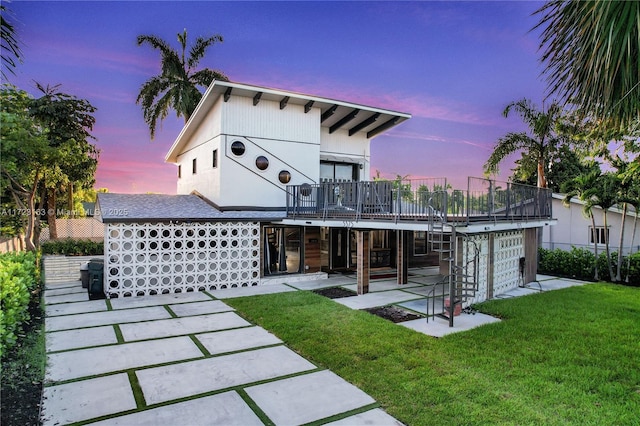 back house at dusk with a lawn, a patio area, and a wooden deck