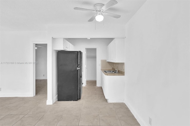 kitchen featuring black refrigerator, tasteful backsplash, ceiling fan, sink, and white cabinets