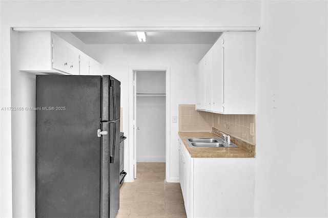 kitchen with tasteful backsplash, white cabinetry, black refrigerator, and sink