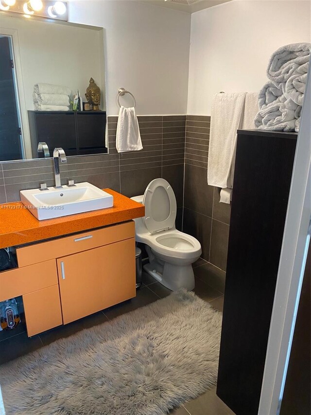 bathroom featuring tile patterned flooring, vanity, toilet, and tile walls