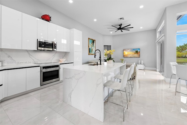 kitchen featuring a kitchen breakfast bar, sink, an island with sink, white cabinetry, and stainless steel appliances