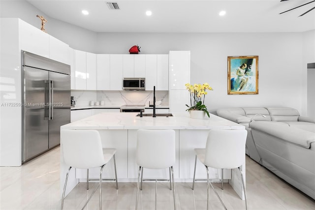 kitchen featuring stainless steel appliances, sink, a center island with sink, white cabinets, and a breakfast bar area