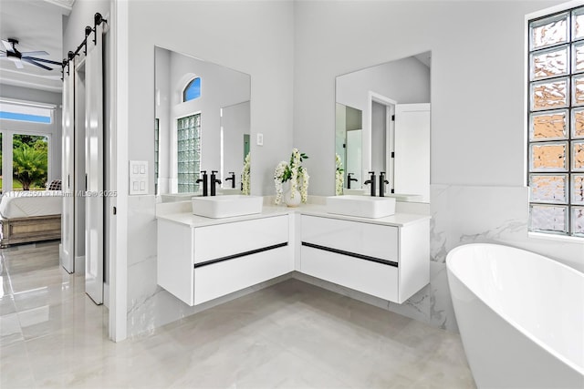 bathroom with a tub to relax in, ceiling fan, vanity, and tile walls