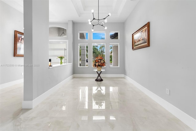 hallway with a notable chandelier and a raised ceiling