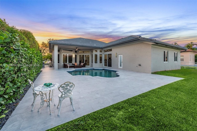 pool at dusk featuring ceiling fan, a patio area, and a lawn