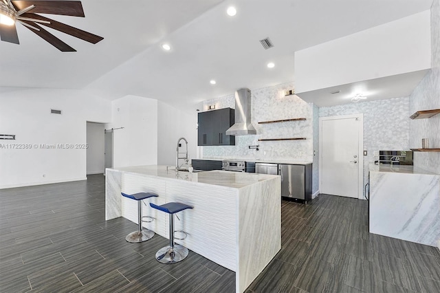 kitchen with ceiling fan, wall chimney range hood, stainless steel range oven, lofted ceiling, and a kitchen bar