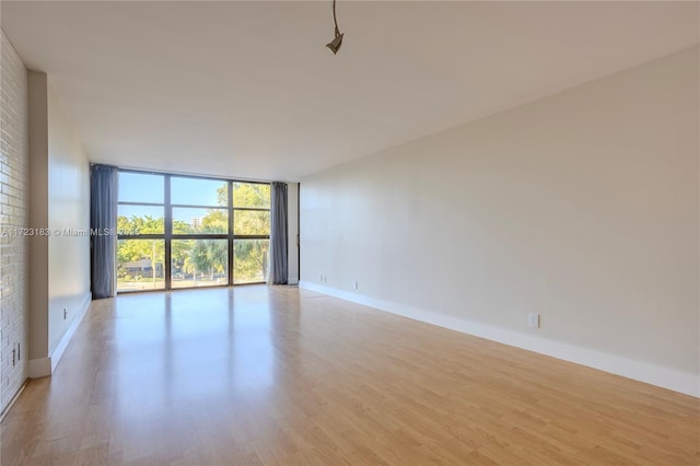 empty room with floor to ceiling windows, light hardwood / wood-style floors, and brick wall