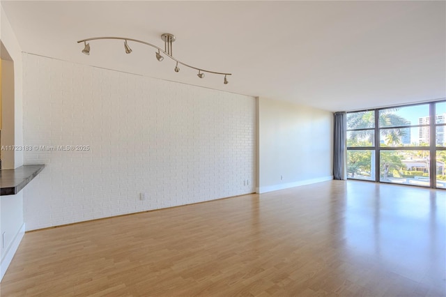 spare room with hardwood / wood-style flooring, a wall of windows, and brick wall