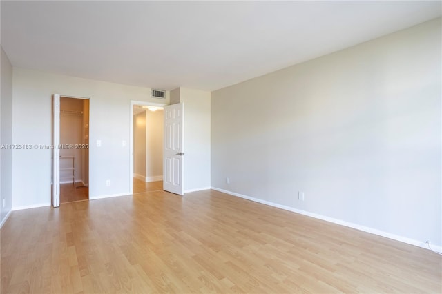 unfurnished bedroom with a walk in closet, a closet, and light wood-type flooring