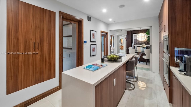 kitchen featuring stainless steel oven, a center island, a breakfast bar area, and light tile patterned floors