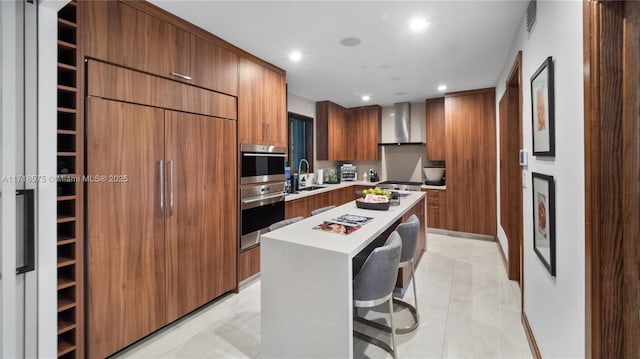 kitchen with sink, a kitchen island, wall chimney exhaust hood, stainless steel appliances, and a breakfast bar area