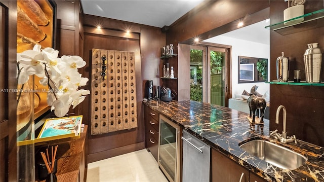 bar with sink, dark brown cabinetry, beverage cooler, and dark stone countertops