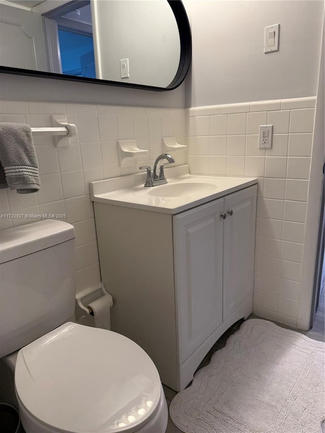 bathroom featuring toilet, vanity, and tile walls