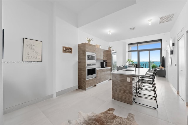 kitchen with stainless steel microwave, sink, wall oven, an island with sink, and a breakfast bar