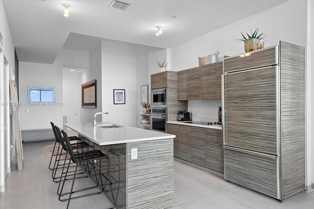 kitchen featuring appliances with stainless steel finishes, a kitchen island with sink, sink, light tile patterned floors, and a breakfast bar area