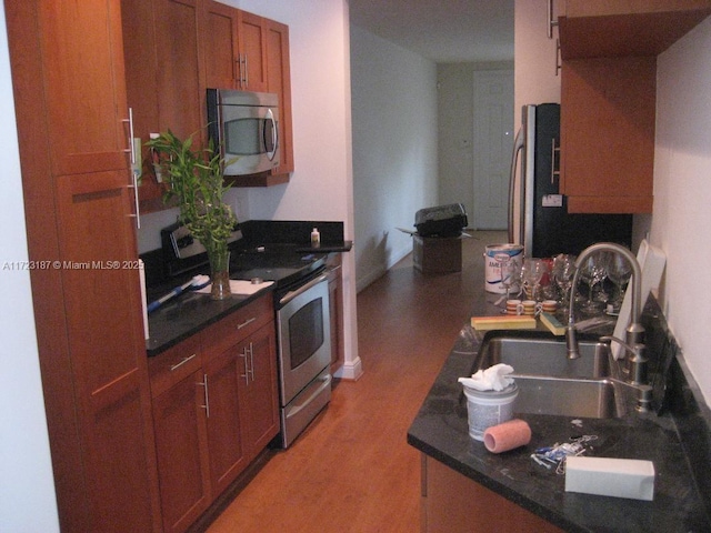 kitchen with dark stone countertops, sink, appliances with stainless steel finishes, and light hardwood / wood-style flooring