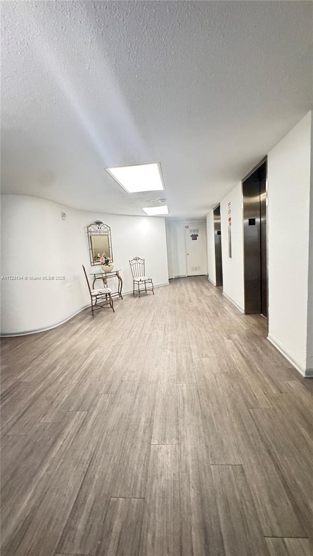 interior space with wood-type flooring, a textured ceiling, and elevator