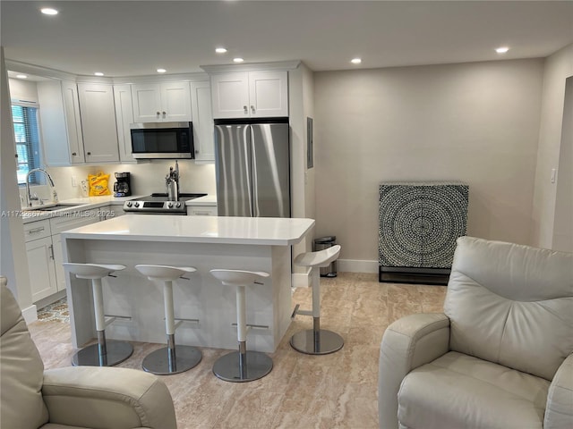 kitchen with a breakfast bar area, appliances with stainless steel finishes, open floor plan, light countertops, and a sink