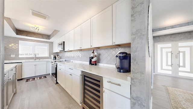 kitchen featuring decorative backsplash, stainless steel appliances, beverage cooler, light hardwood / wood-style flooring, and white cabinets