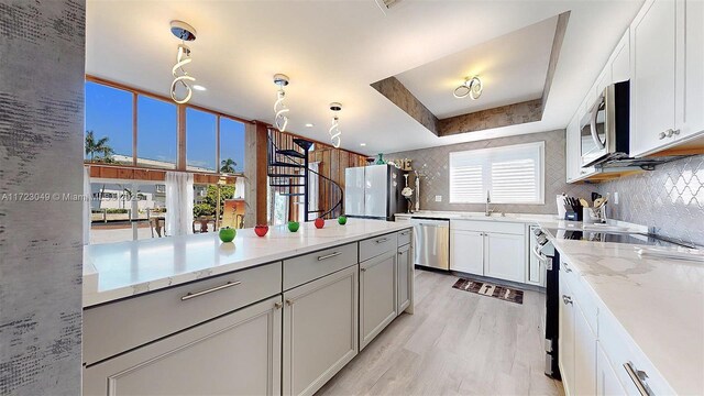 kitchen featuring white cabinets, a raised ceiling, sink, light stone countertops, and appliances with stainless steel finishes