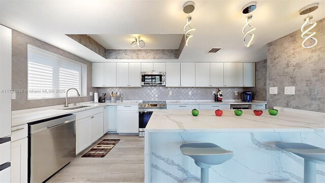 kitchen with sink, pendant lighting, a kitchen bar, white cabinets, and appliances with stainless steel finishes