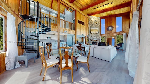 dining room featuring wooden ceiling, a high ceiling, a stone fireplace, beamed ceiling, and hardwood / wood-style floors