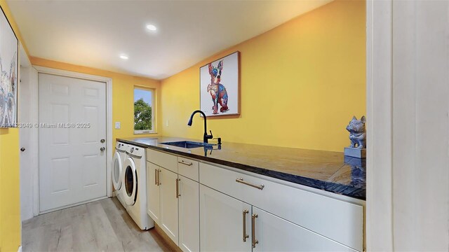 clothes washing area with cabinets, light wood-type flooring, separate washer and dryer, and sink