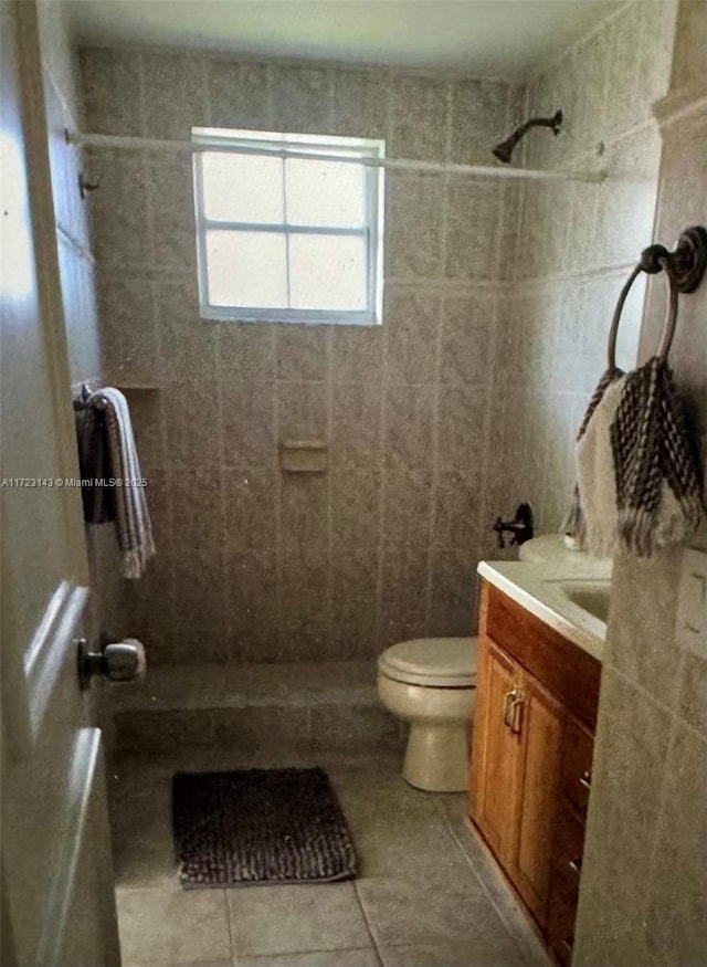 bathroom with tile patterned flooring, vanity, toilet, and tiled shower