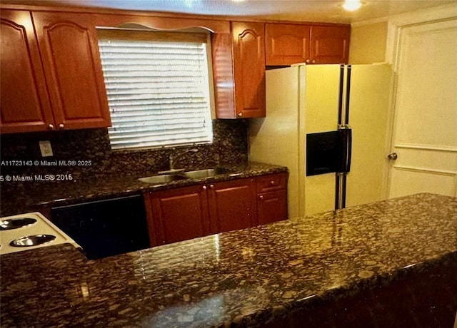 kitchen featuring white refrigerator with ice dispenser, dark stone counters, sink, black dishwasher, and tasteful backsplash