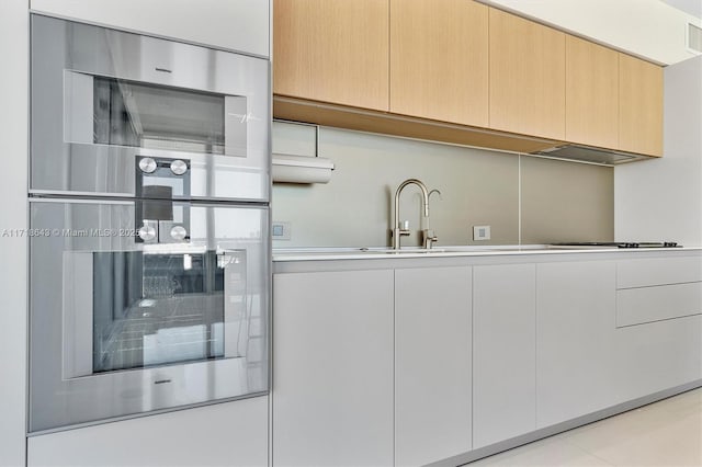 kitchen featuring light brown cabinetry, white gas stovetop, stainless steel double oven, ventilation hood, and sink