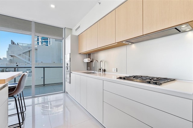 kitchen with sink, light brown cabinets, expansive windows, stainless steel gas stovetop, and light tile patterned flooring