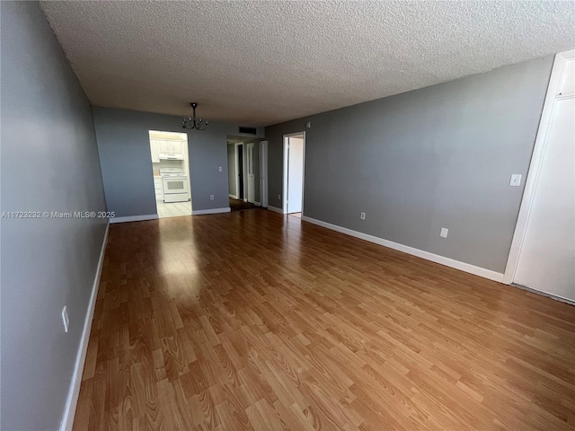 spare room with a textured ceiling, light hardwood / wood-style floors, and an inviting chandelier