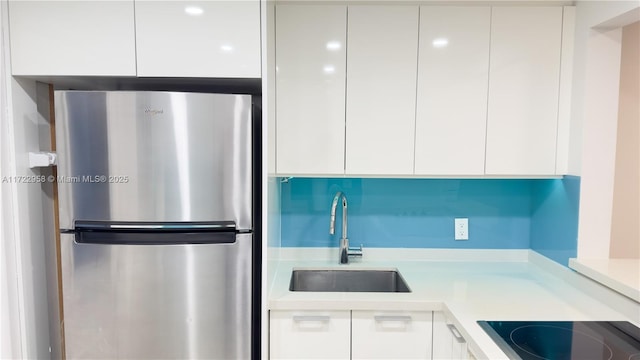 kitchen featuring cooktop, white cabinetry, sink, and stainless steel refrigerator