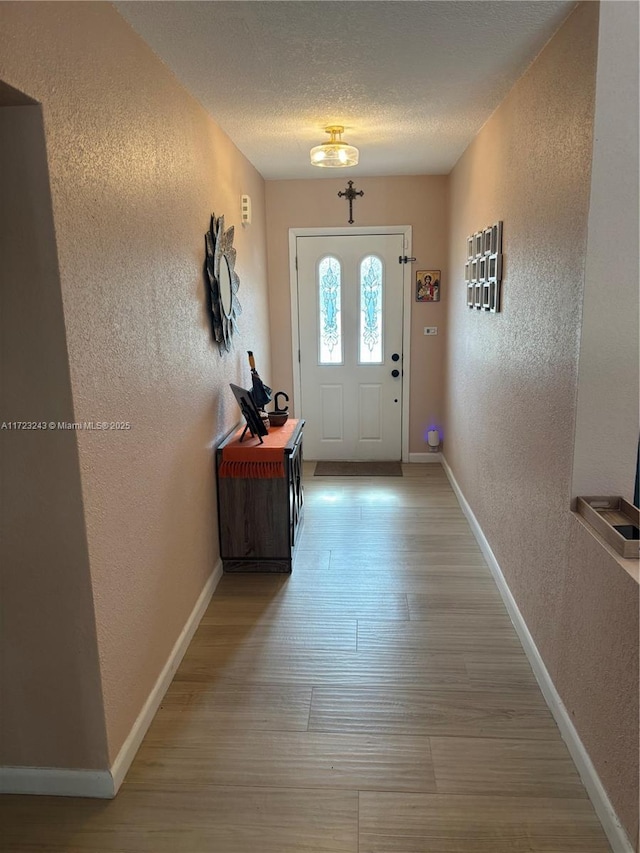 entryway featuring light wood-type flooring, a textured wall, a textured ceiling, and baseboards