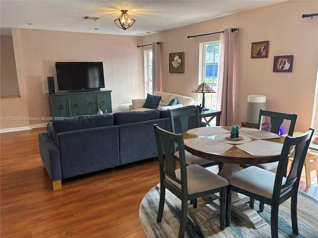 dining area with baseboards, a textured ceiling, visible vents, and wood finished floors