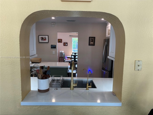 kitchen with arched walkways, light countertops, visible vents, a textured wall, and freestanding refrigerator