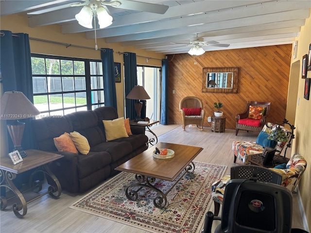 living room with wooden walls, beamed ceiling, light wood-style flooring, and a ceiling fan