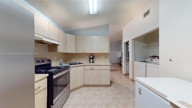 kitchen with a textured ceiling, light tile patterned floors, stainless steel range with electric stovetop, sink, and separate washer and dryer