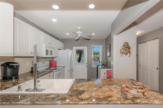 kitchen with kitchen peninsula, white cabinets, dark stone counters, and white appliances