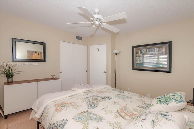 bedroom with ceiling fan, a closet, light tile patterned flooring, and a textured ceiling