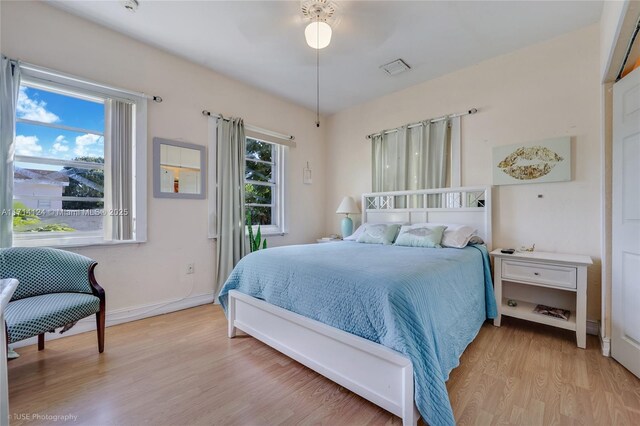 bedroom featuring ceiling fan, light hardwood / wood-style floors, and multiple windows