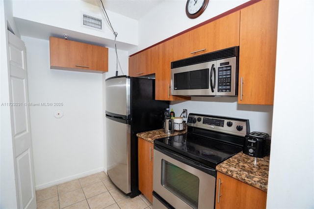 kitchen with dark stone countertops, light tile patterned floors, and stainless steel appliances