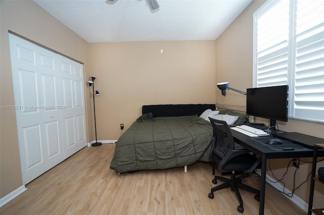 bedroom with ceiling fan, a closet, light hardwood / wood-style flooring, and a textured ceiling