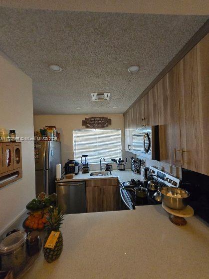 21340 NE 8th Ct Unit 1, Miami, FL 33179 - kitchen featuring appliances with stainless steel finishes, a sink, light countertops, brown cabinets, and a textured ceiling