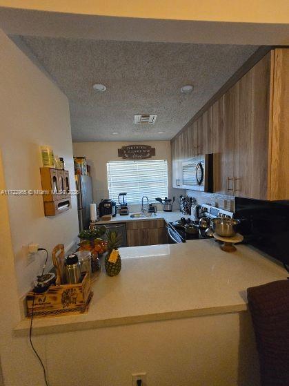 21340 NE 8th Ct Unit 1, Miami, FL 33179 - kitchen with light countertops, appliances with stainless steel finishes, a sink, brown cabinets, and recessed lighting