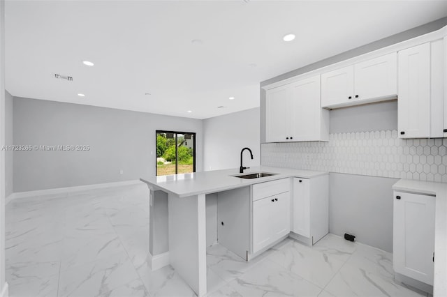 kitchen with white cabinets, backsplash, kitchen peninsula, and sink