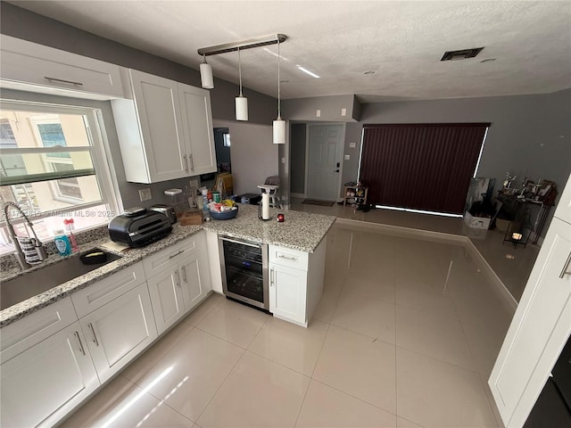 kitchen with kitchen peninsula, a textured ceiling, beverage cooler, decorative light fixtures, and white cabinetry