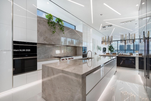 kitchen featuring stone countertops, white cabinets, sink, black oven, and a large island