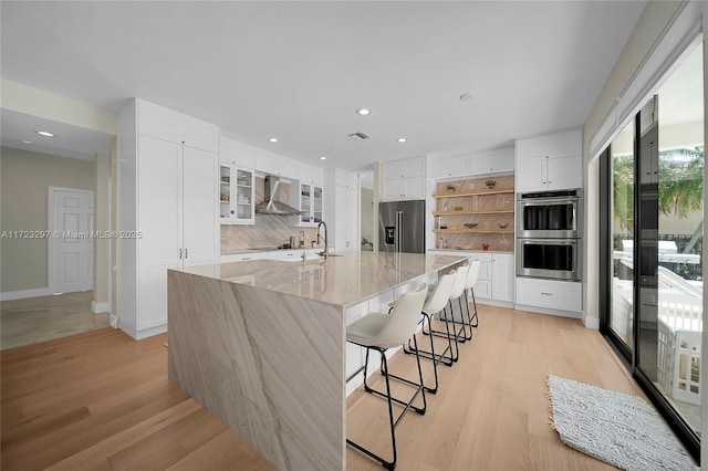 kitchen with a spacious island, white cabinets, wall chimney range hood, stainless steel appliances, and a breakfast bar area